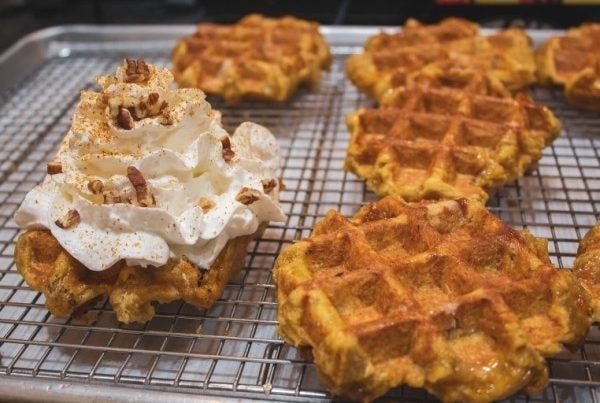 A plate of golden brown waffles with one topped with whipped cream and pecans for Sunday brunch