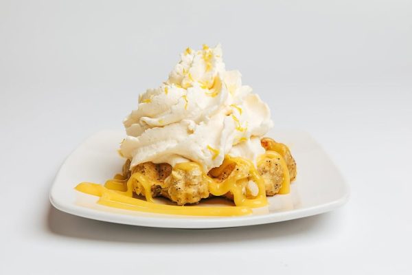 Lemon waffle topped with whipped cream, lemon curd, and zest, drizzled with a sweet glaze.