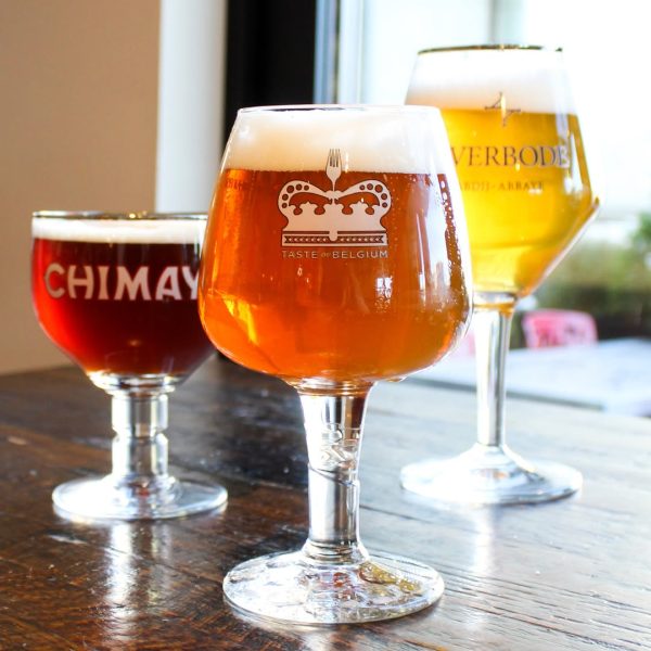 Three Belgian beers, Chimay, Taste of Belgium, and Averbode, served in signature glassware on a wooden table.