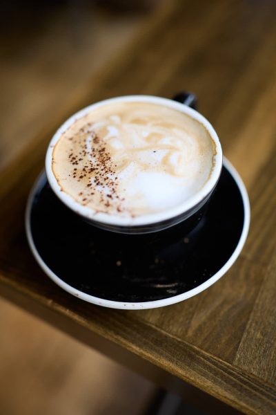 A close-up of a cappuccino in a black cup and saucer, topped with foamy milk and a dusting of cocoa powder.