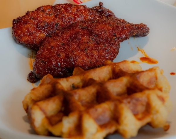 Chicken and waffles from Taste of Belgium placed on a wooden table with a side of cut vegetable salad.