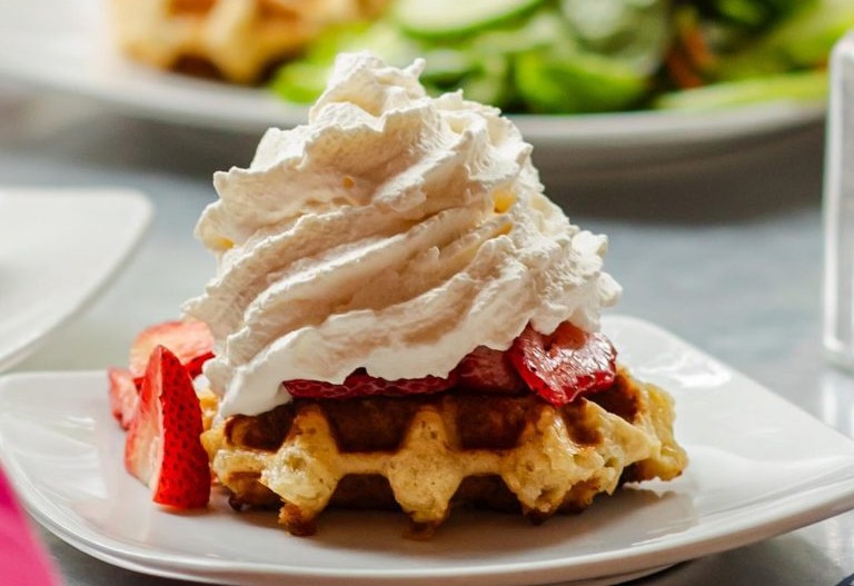 A golden Belgian waffle topped with fresh strawberries and sweet whipped cream, served as a simple yet indulgent brunch treat.
