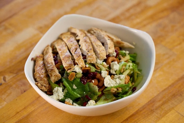 A fresh salad topped with grilled chicken, blue cheese crumbles, dried cranberries, and nuts.