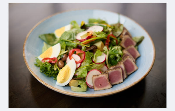 Nicoise salad with seared tuna, hard-boiled eggs, olives, radishes, and greens in a light blue bowl.
