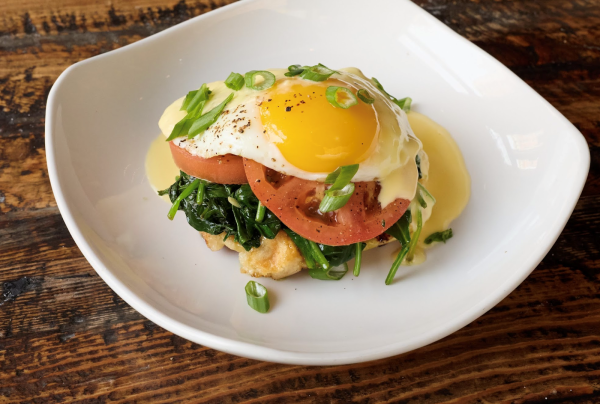 Brunch dish with egg, tomatoes, greens, and hollandaise on a waffle, garnished with scallions on a white plate, served at ToB.