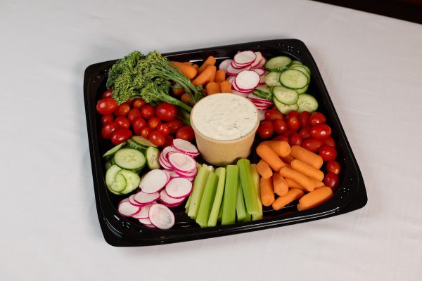 A salad with cherry tomatoes, baby carrots, celery sticks, and more vegetables, with a cup of ranch dip, on a plate.
