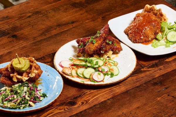 Three plates of fried chicken and waffles on a wooden table at Taste of Belgium in Cincinnati.